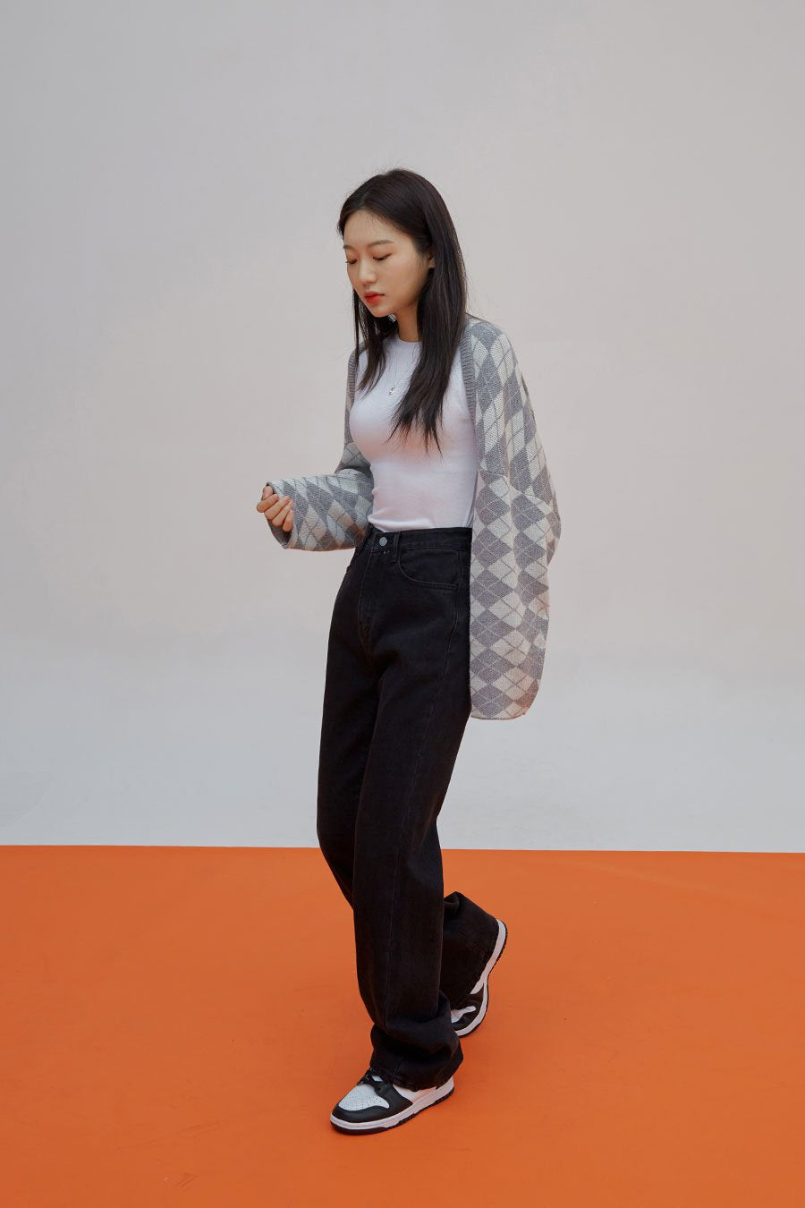 Straight Leg Pants J23 in black, three-quarter front side view on model looking down, straight-leg cotton denim, high waist, styled with argyle open cardigan and sneakers.