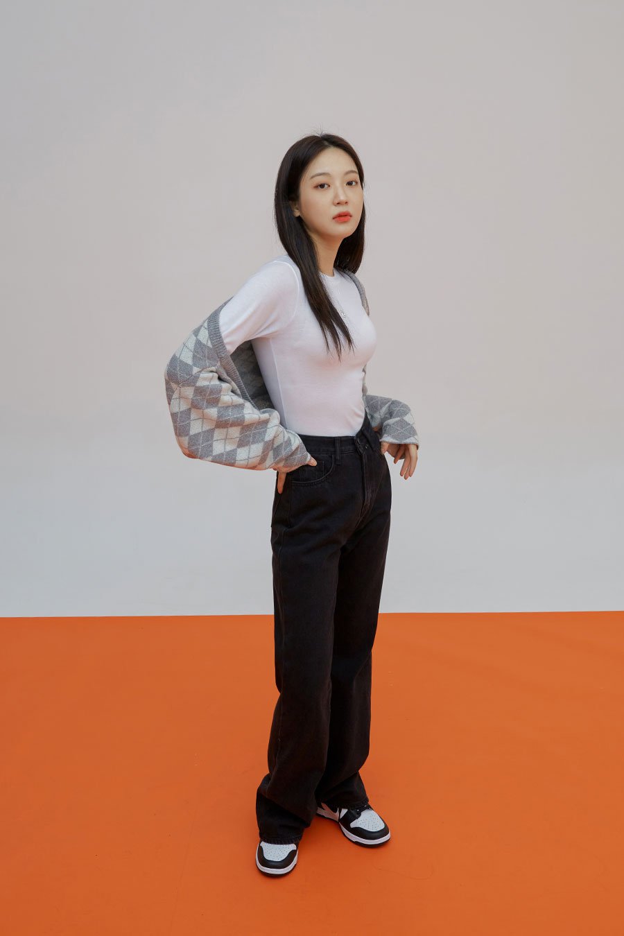Straight Leg Pants J23 in black, full-length side-angled shot on model, straight-fit long cotton denim, high waist, hand in pocket, styled with argyle cardigan and white tee.