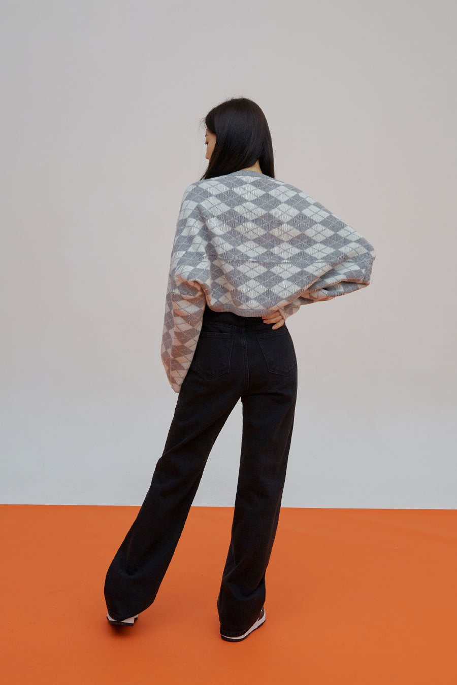 Straight Leg Pants J23 in black, back full-length view on model, straight cotton denim with two back pockets, high waist, paired with argyle sweater, sneakers at hem.