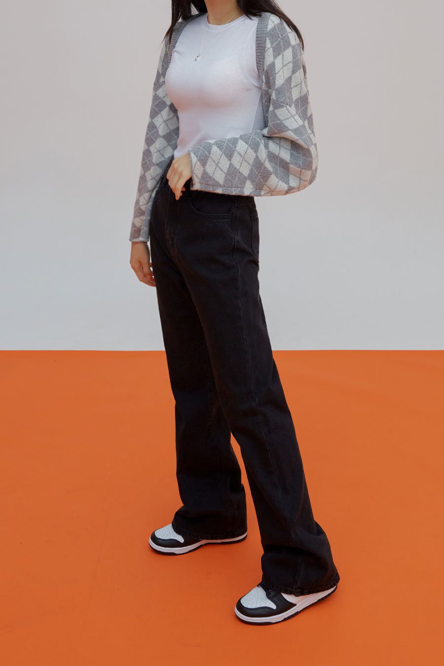 Straight Leg Pants J23 in black, side full-length view on model, straight-leg long cotton denim, high-rise fit, hand in pocket, styled with argyle cardigan and white tee.