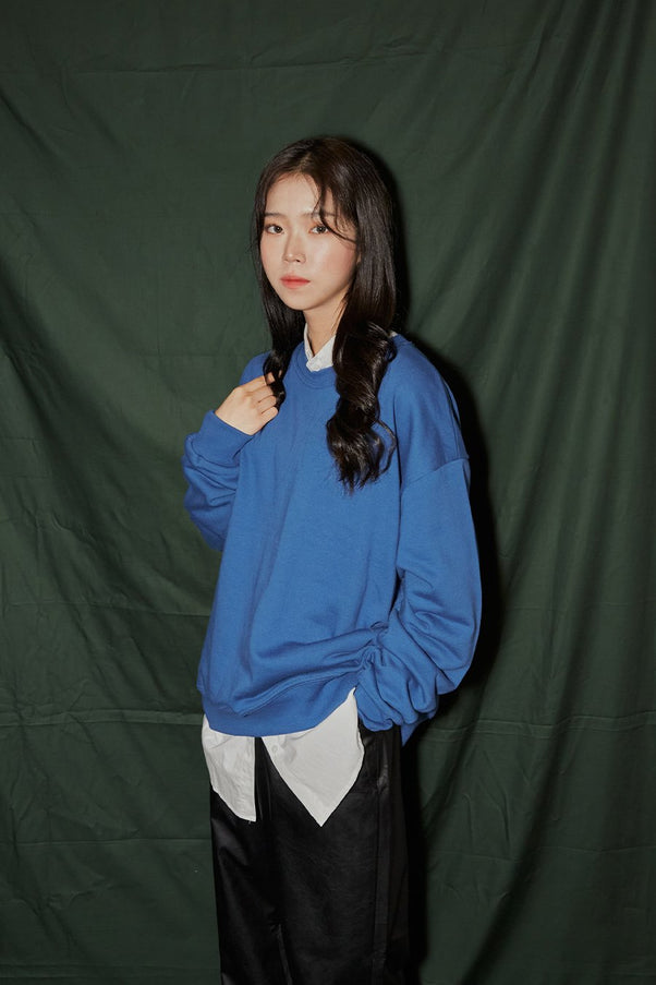 Loose Fit Sweatshirt F6 in blue, three-quarter side close-up on model, round neck and drop-shoulder silhouette visible, layered over white shirt hem, paired with black faux-leather wide-leg pants.
